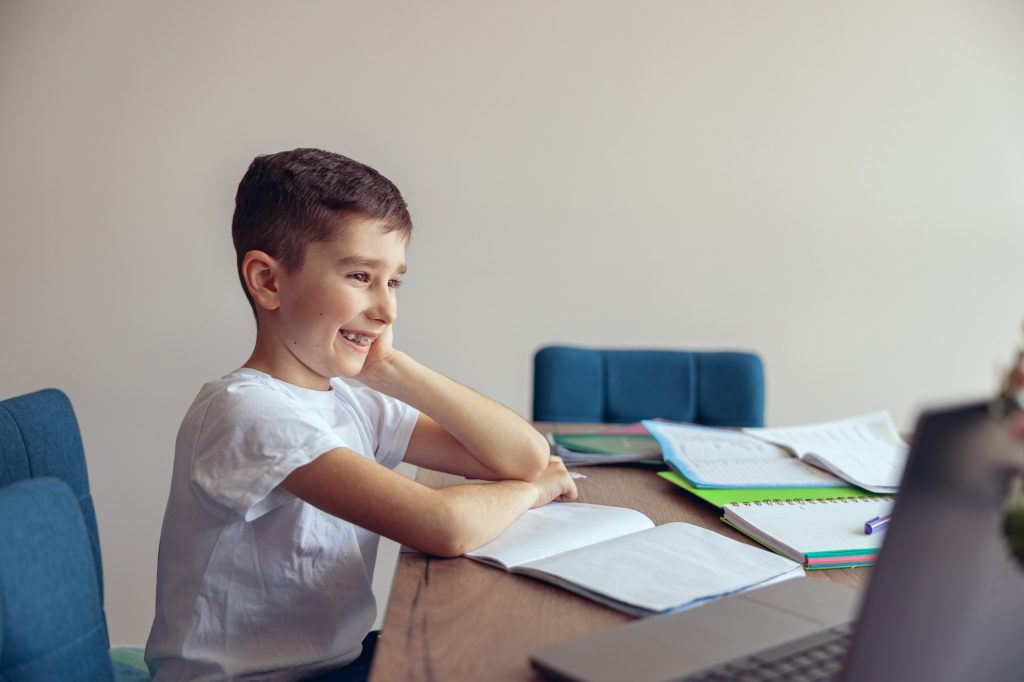 Happy cheerful schoolboy with braces watching online lesson on laptop and smiling.