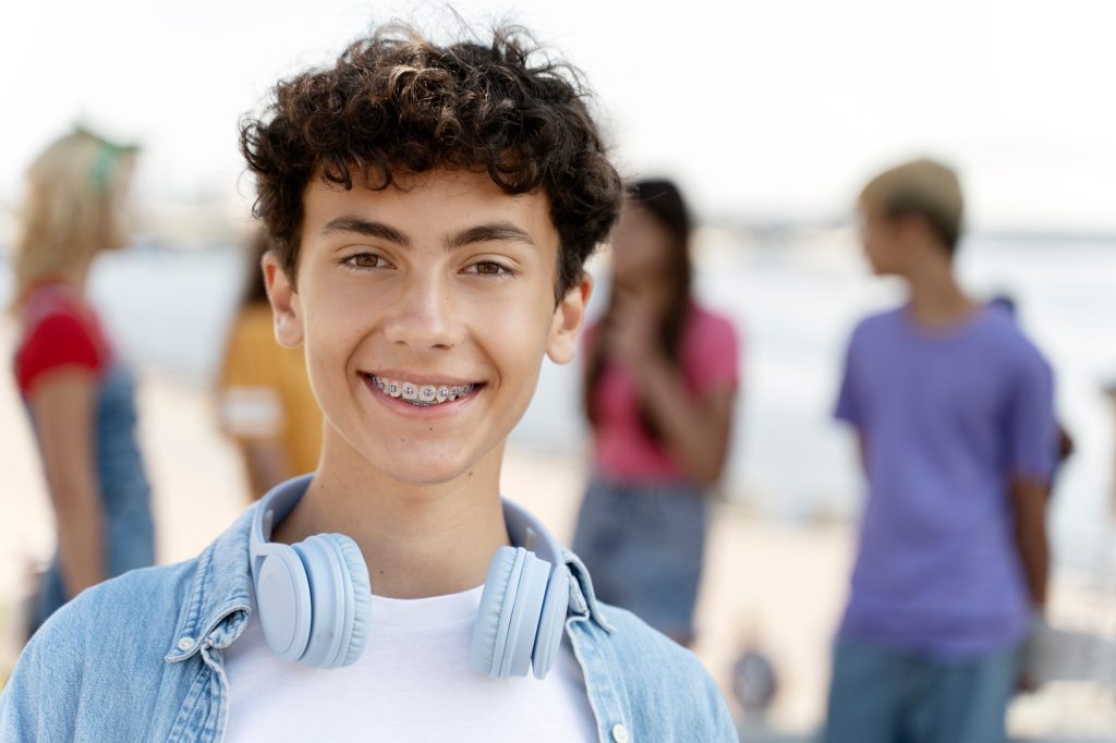 Portrait of smiling teenager with braces wearing headphones looking at camera standing on the street