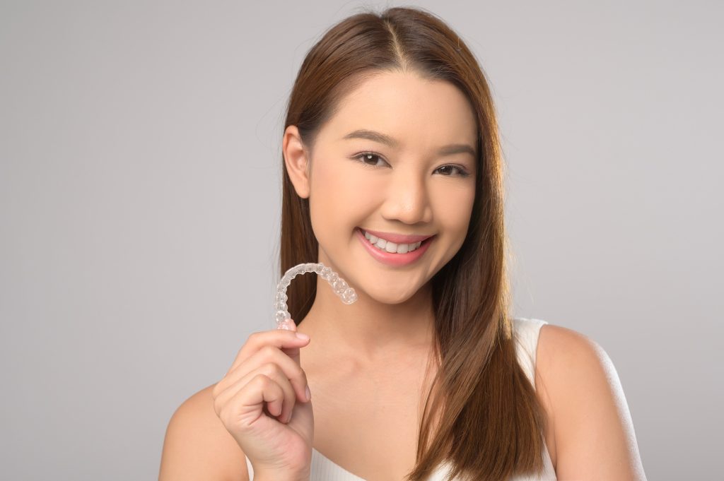 Smiling woman holding invisalign braces over white background